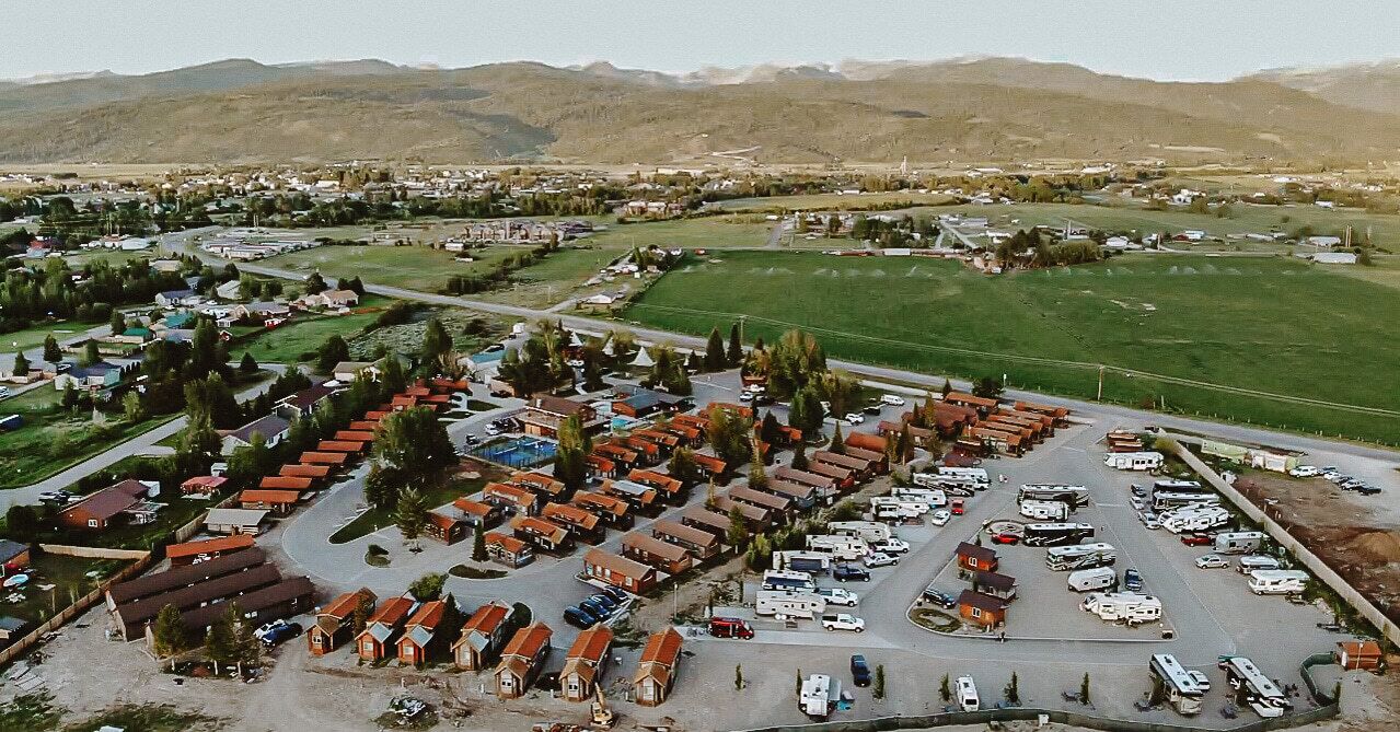An aerial view of a residential area with multiple houses, a parking lot, and a green field.