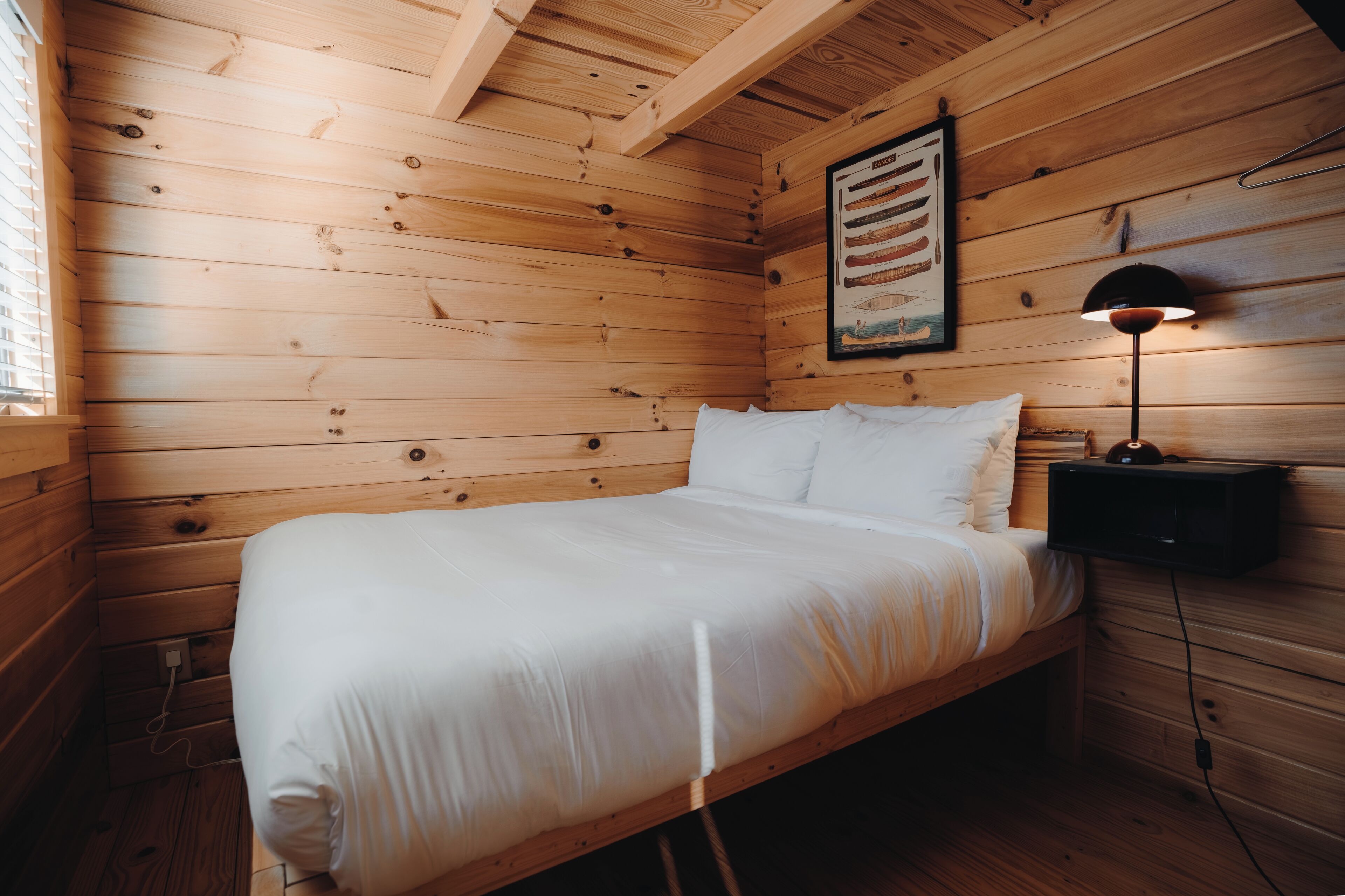 A wooden cabin-style bedroom with a bed, a nightstand, a lamp, and a framed picture on the wall.