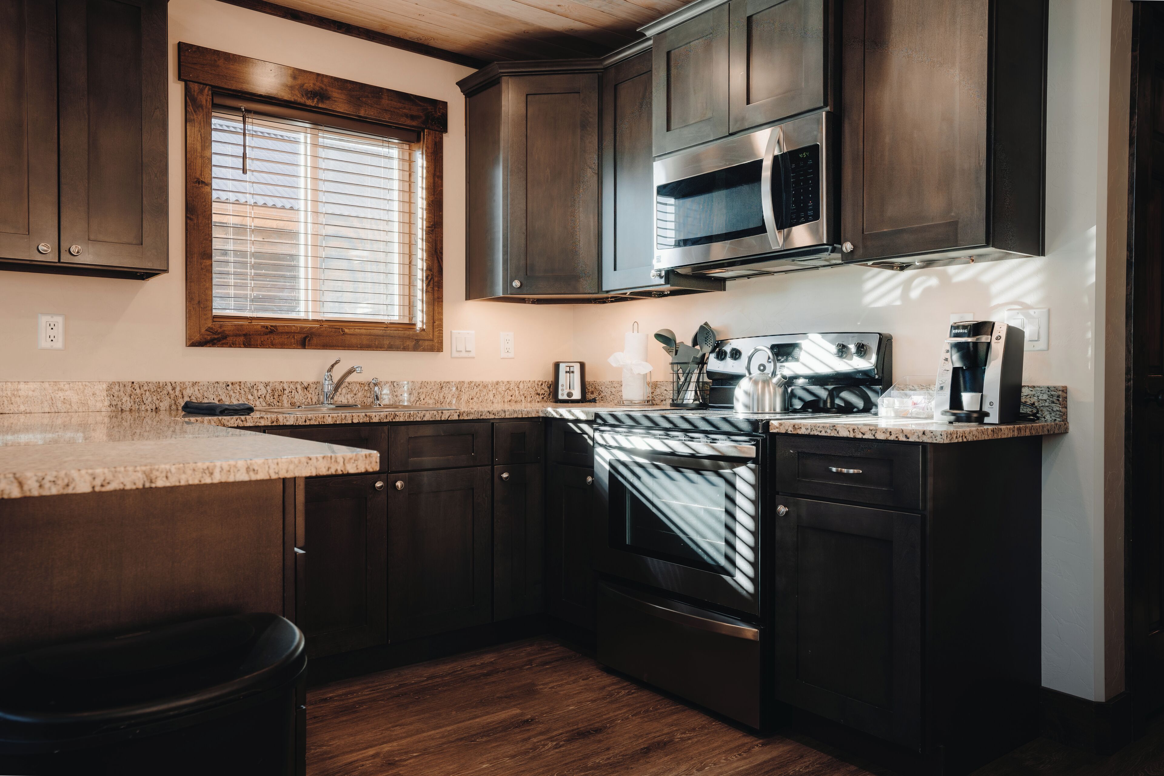 A kitchen with dark wooden cabinets, a stainless steel microwave, a built-in oven, and a granite countertop.