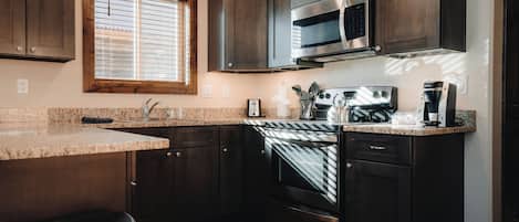 A kitchen with dark wooden cabinets, a stainless steel microwave, a built-in oven, and a granite countertop.