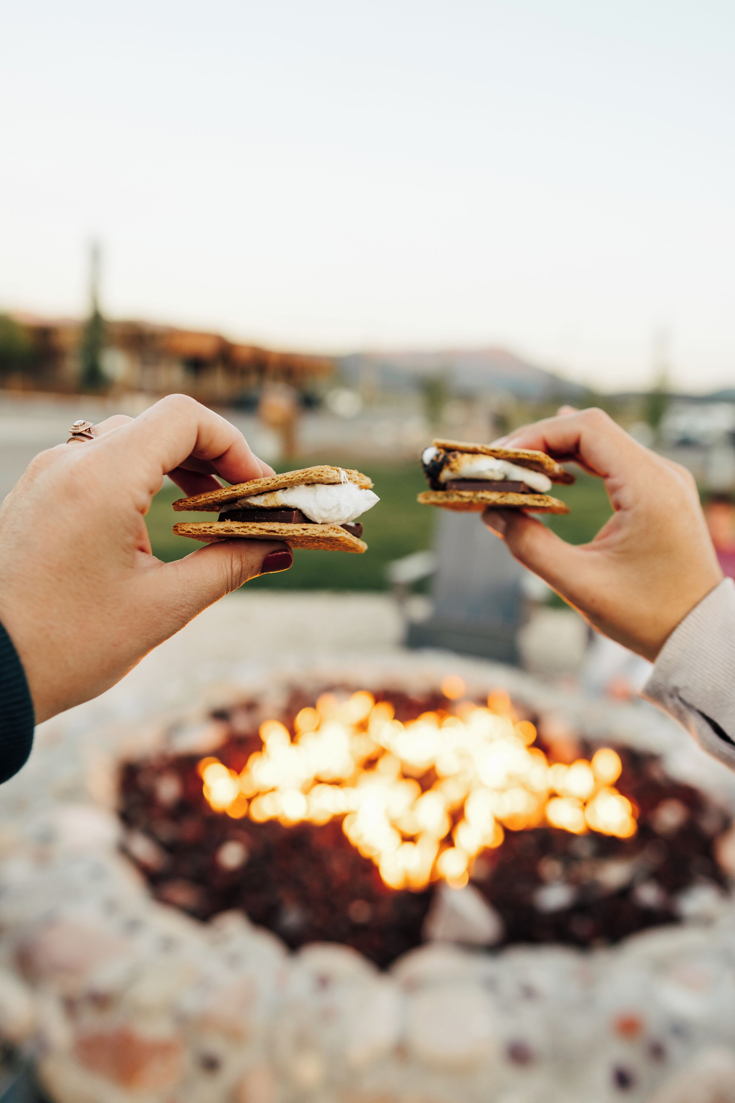 Two hands holding a s'more over a campfire.
