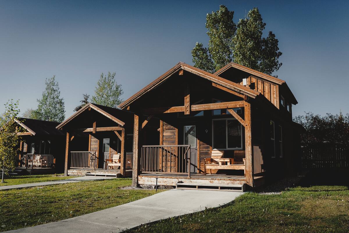 A wooden cabin with a porch, a covered deck, and a clear view of the surrounding trees.