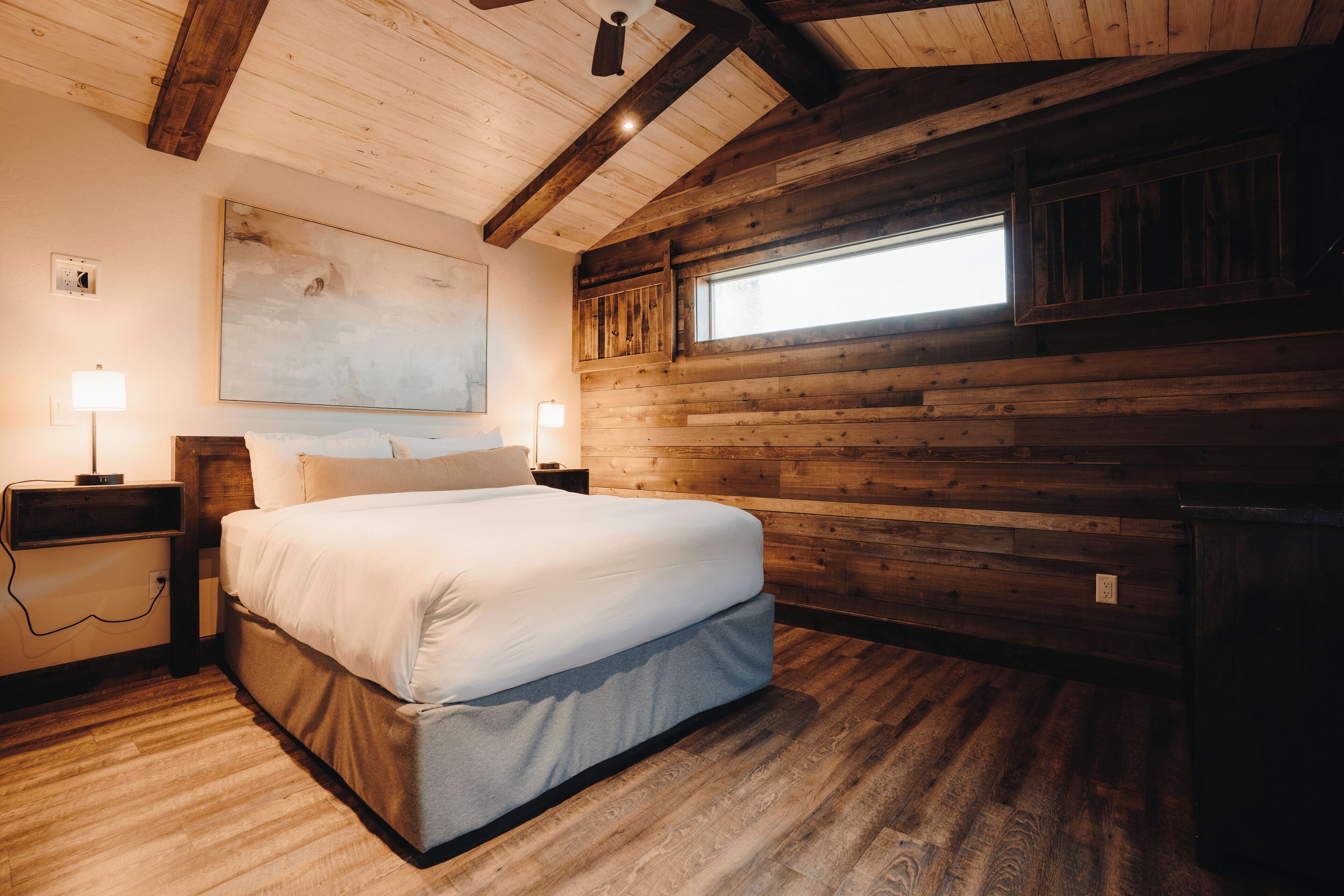Une chambre dotée d’un grand lit, de murs en bois, d’un ventilateur de plafond et d’une fenêtre laissant entrer la lumière naturelle.
