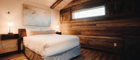 Une chambre dotée d’un grand lit, de murs en bois, d’un ventilateur de plafond et d’une fenêtre laissant entrer la lumière naturelle.