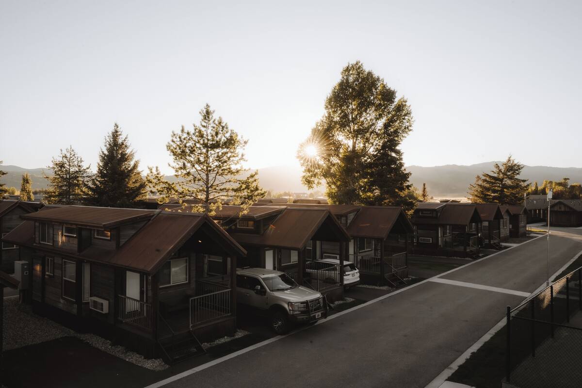A row of cabins with a road in front, surrounded by trees and a mountain in the background.