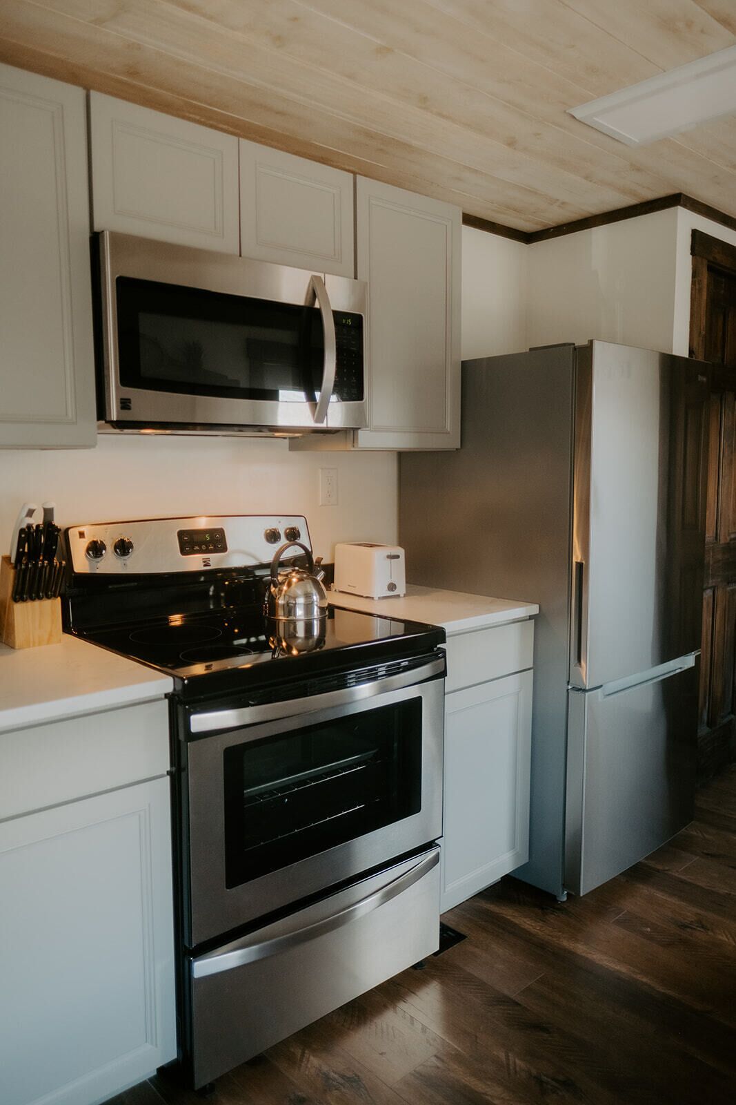A modern kitchen with stainless steel appliances, wooden flooring, and white cabinetry.