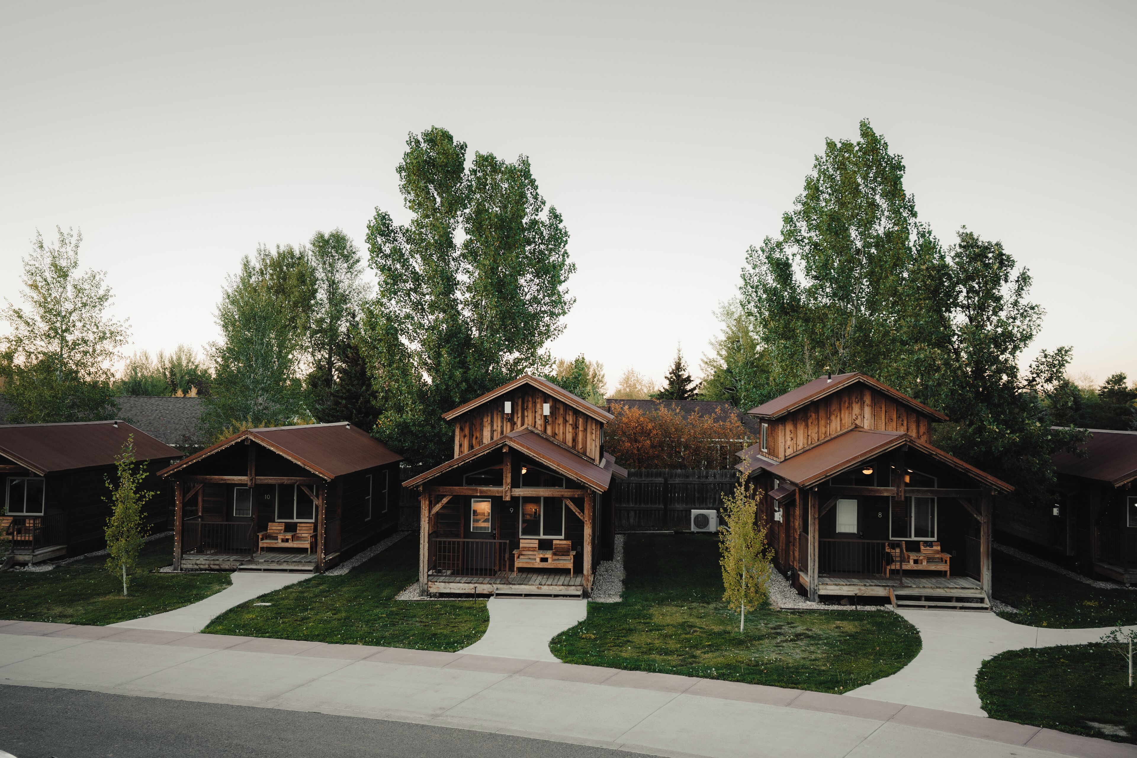 A row of wooden cabins with porches, each featuring a bench and a small table.
