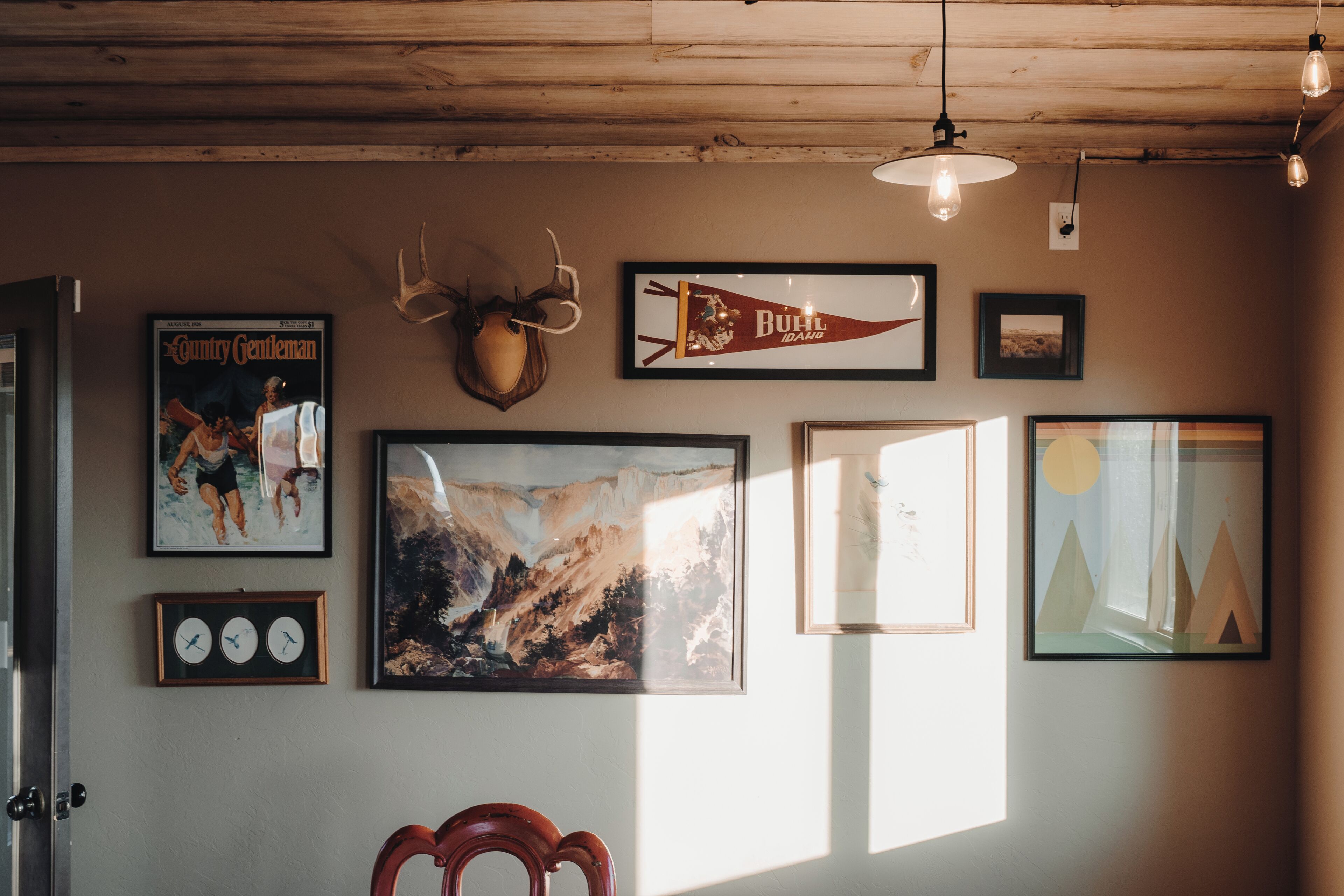 A room with wooden ceiling beams, framed artwork, and a mounted deer head.