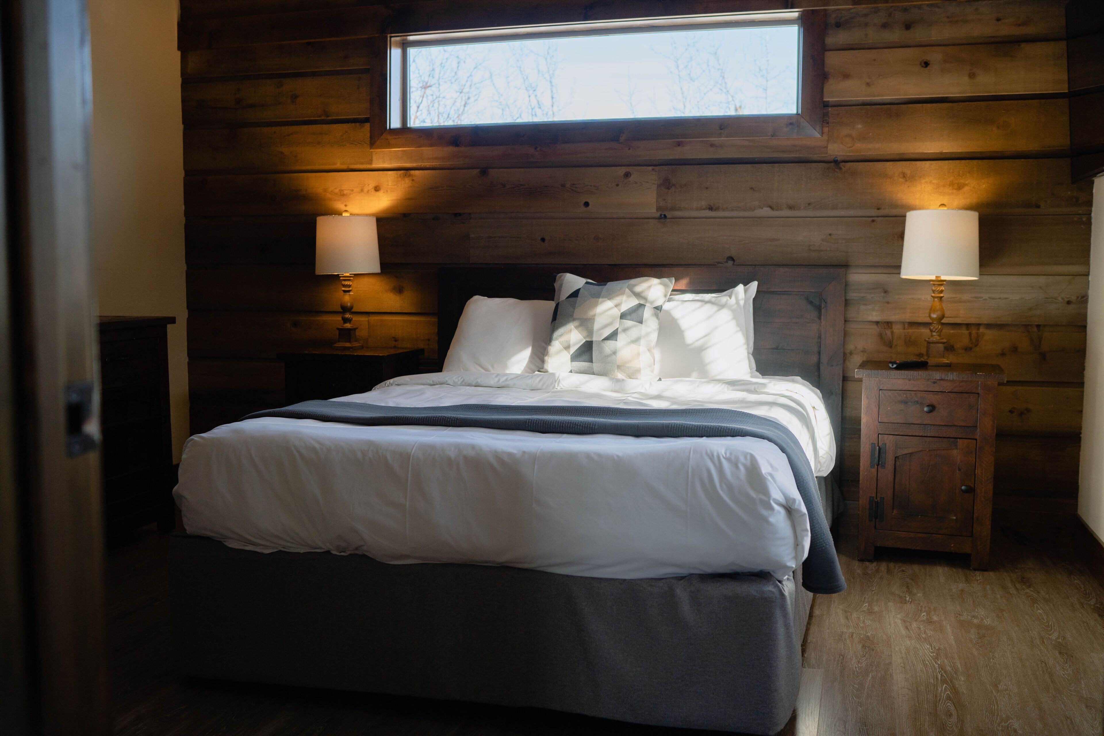 A wooden-paneled bedroom with a bed, two bedside tables, and a window above the bed.