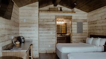 A wooden cabin interior with a kitchenette, two beds, a dining area, and a bathroom.