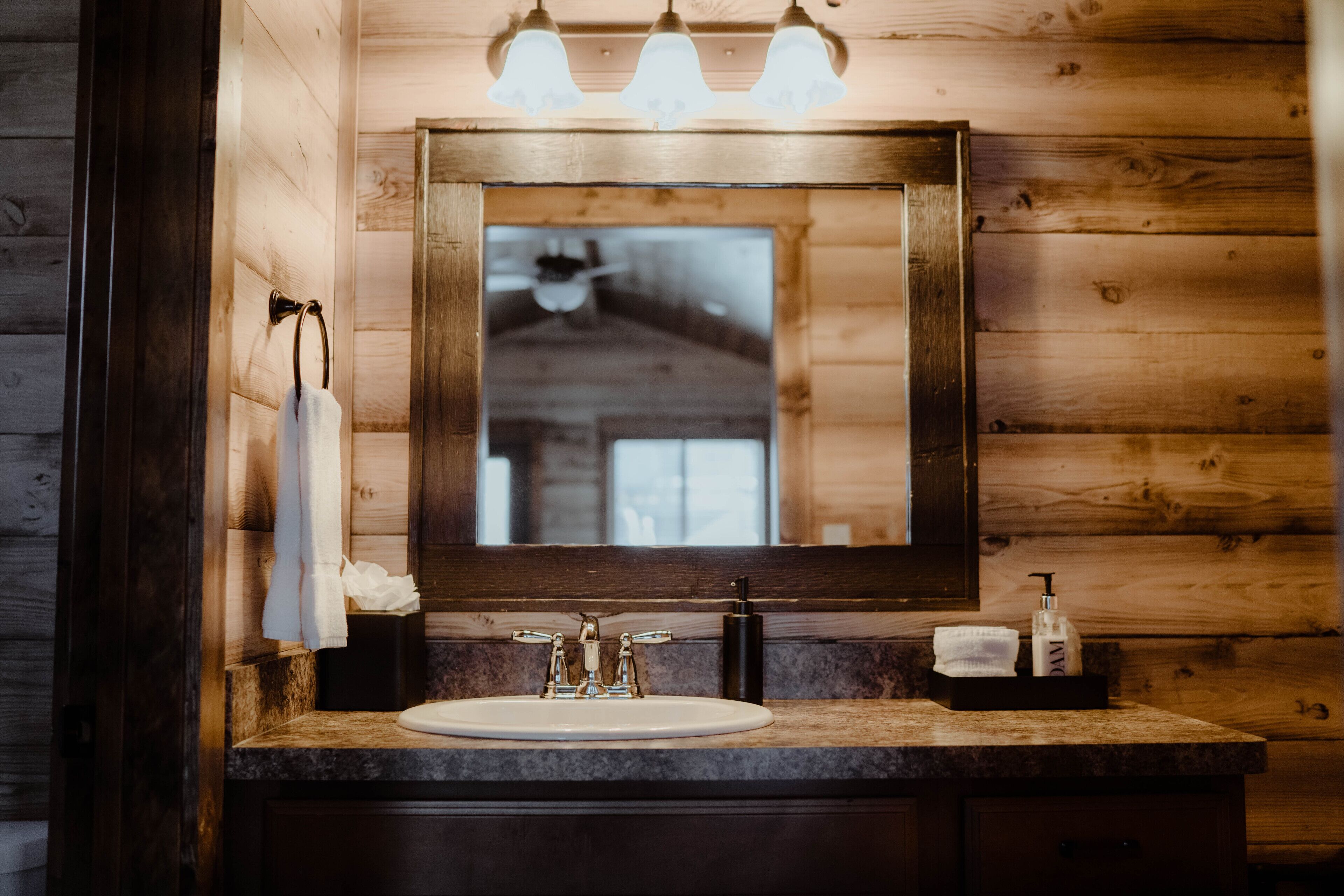 A wooden cabin-style bathroom with a large mirror, a sink, and a towel rack.