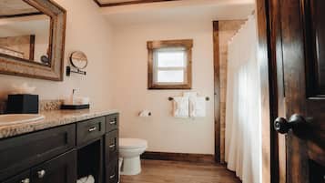 A bathroom with a wooden vanity, a large mirror, a small window, and a door leading to a shower area.