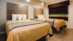 A hotel room with two beds, each with a patterned bedspread and white pillows. There is a window with striped curtains and a wooden headboard. - Palace Inn Beltway 8 & Veterans Memorial (Houston)