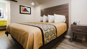 A hotel room with a bed, a bedside table, a lamp, and a painting on the wall. - Palace Inn Beltway 8 & Veterans Memorial (Houston)
