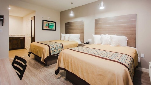 A hotel room with two beds, a desk, a chair, a small kitchenette, and a painting on the wall. - Palace Inn Beltway 8 & Veterans Memorial (Houston)