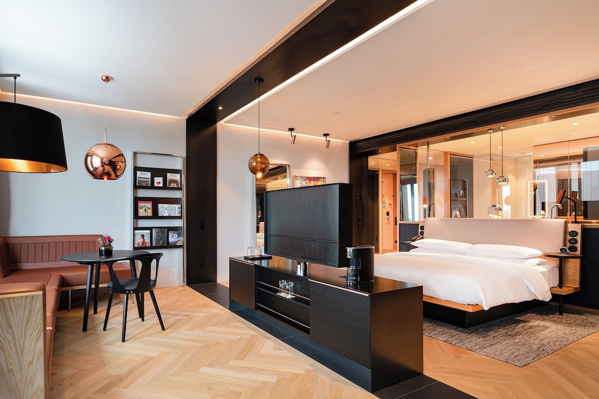Un dormitorio moderno con cama, mesita de noche, televisor y zona de estar con mesa y sillas.