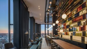 A modern bar area with a long counter, multiple stools, and a large wine display. - ANDAZ MUNICH SCHWABINGER TOR, BY HYATT (Munich)