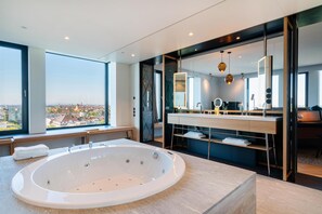 Un baño moderno con una bañera grande, un tocador con espejo y vistas a la ciudad.