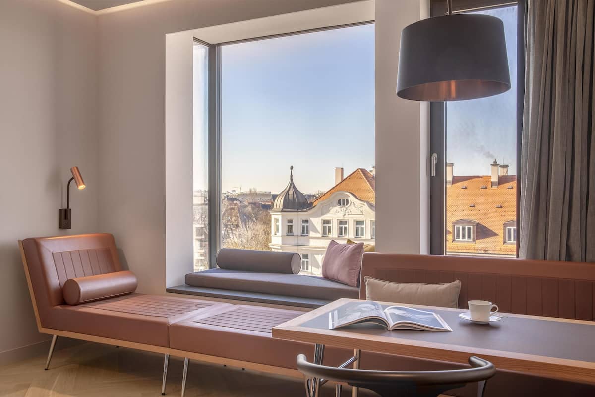 Una habitación moderna con un ventanal grande, un sofá, una mesa con un libro y una lámpara.