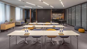 A modern conference room with multiple tables, chairs, and a kitchenette area.