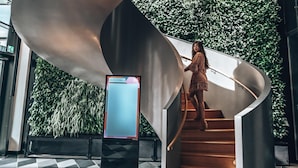A modern interior with a curved staircase, a digital display, and a green wall. - ANDAZ MUNICH SCHWABINGER TOR, BY HYATT (Munich)