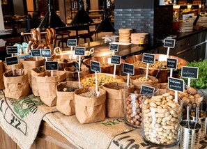 Variedad de nueces y frutas secas expuestas en bolsas de papel con etiquetas, dispuestas sobre una mesa en un café.