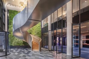 Un interior moderno con una escalera de caracol, una pared verde y grandes puertas de cristal que dan a un comedor.