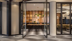 A modern interior with a checkered floor, a wooden dining table with chairs, and a glass partition separating the dining area from a seating area with lamps. - ANDAZ MUNICH SCHWABINGER TOR, BY HYATT (Munich)