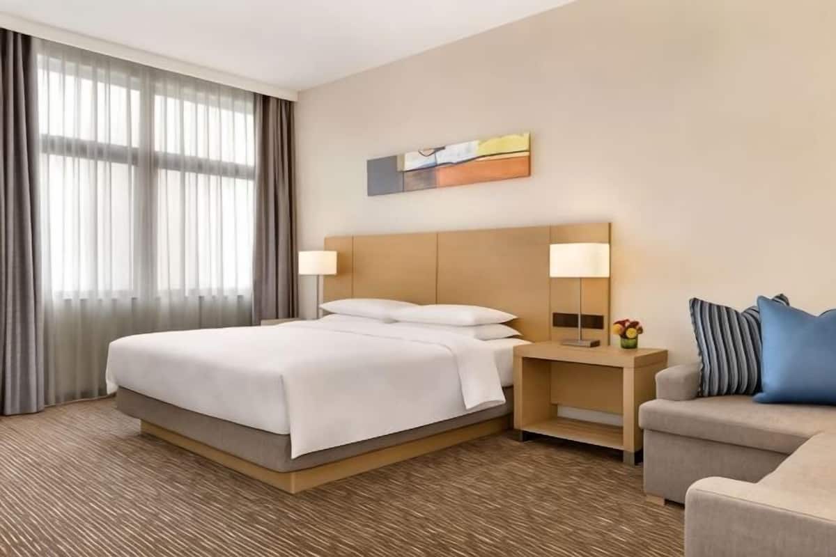 A hotel room with a large bed, bedside lamps, a desk, a chair, and a painting on the wall.