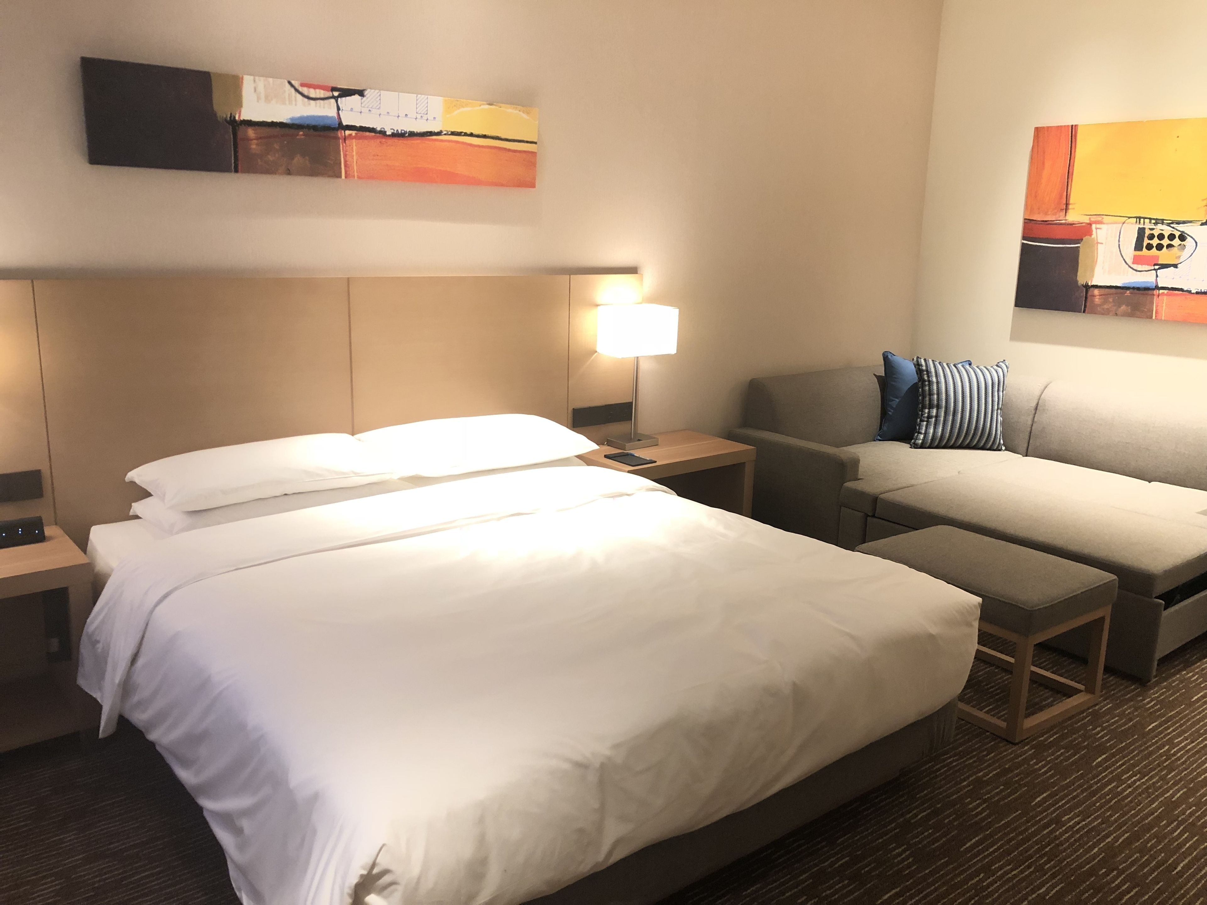 Una habitación de hotel con una cama grande, una mesita de noche con lámpara, un sofá y una pequeña mesa.