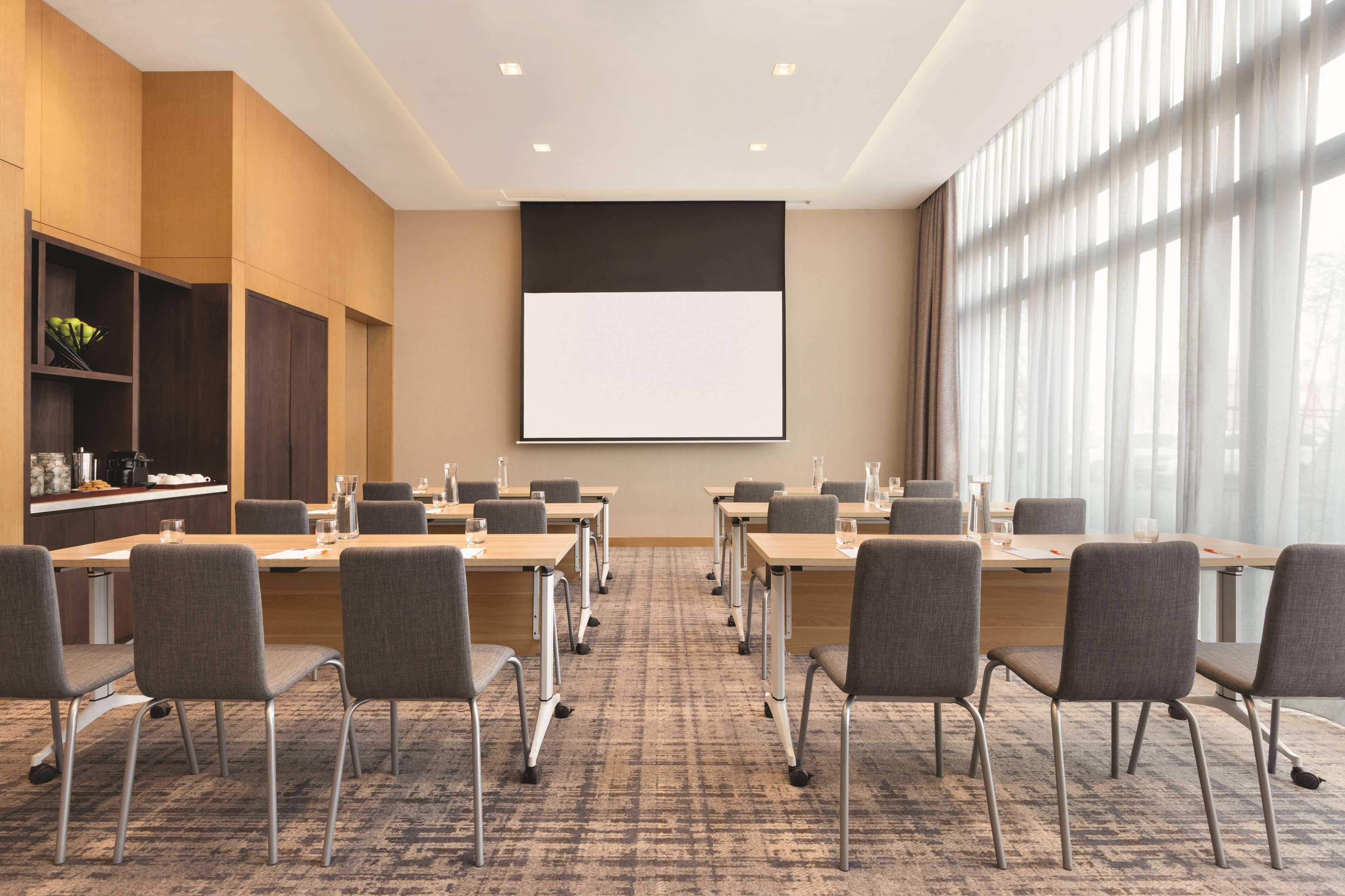 A conference room with a large screen, multiple tables, and chairs arranged for meetings.