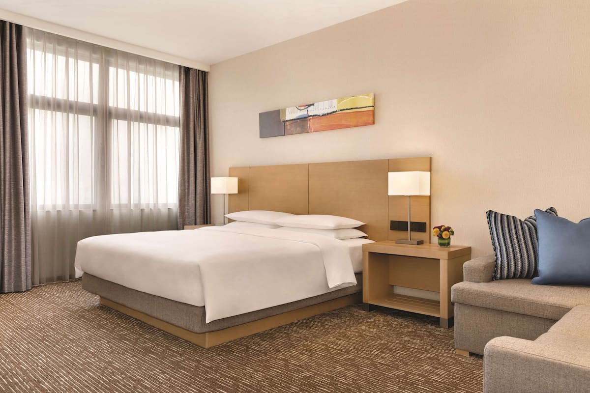 A hotel room with a large bed, two bedside lamps, a small table with a vase of flowers, and a couch.