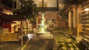 Un bâtiment à plusieurs niveaux doté d’un élément aquatique central, d’un espace extérieur aménagé pour s’asseoir et d’un jardin bien entretenu.