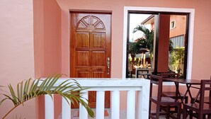 Une porte en bois surmontée d’une arche décorative, une balustrade blanche et un patio aménagé avec des meubles en bois et un sol carrelé.