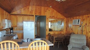 A cabin-style kitchen with wooden walls, a refrigerator, a sink, and a dining area with a table and chairs.
