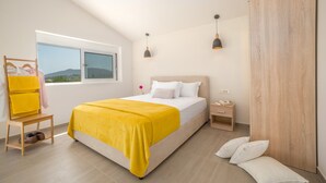 Een slaapkamer met een bed, nachtkastje, houten kledingkast, raam met uitzicht en een stoel met gele handdoeken.