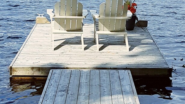 Un muelle de madera con dos sillas Adirondack y una planta en maceta.