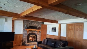 Un salón acogedor con chimenea de piedra, vigas de madera, un sofá de cuero y un televisor.