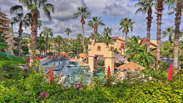 Um resort com piscina, palmeiras e uma construção de palha.