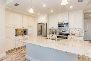 A modern kitchen with white cabinetry, a granite countertop, stainless steel appliances, and pendant lighting.