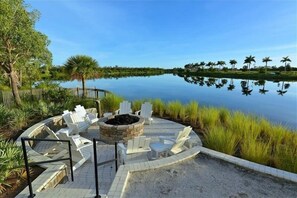 Relax by the fire pit in a serene lakeside setting surrounded by lounge chairs and palm trees.