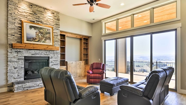 A spacious living room with a stone fireplace, leather sofas, a red chair, and a balcony with a view. - Chic Willamette Valley Home w/ Deck & Vineyard! (Gaston)