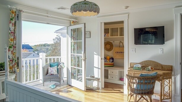 A room with a view of a house, a wicker chair, a table, and a television on the wall. - Spend your quintessential Cape Cod vacation, in a beautifully renovated 1862 Farm House on Stage Harbor Road! (Chatham)
