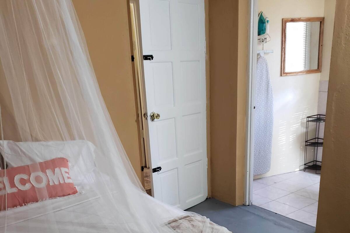 A bedroom with a bed covered in a white canopy, a 'WELCOME' pillow, and a door leading to a bathroom.