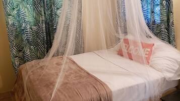 Una cama con dosel, un almohadón rosa con el texto "WELCOME" y cortinas estampadas.