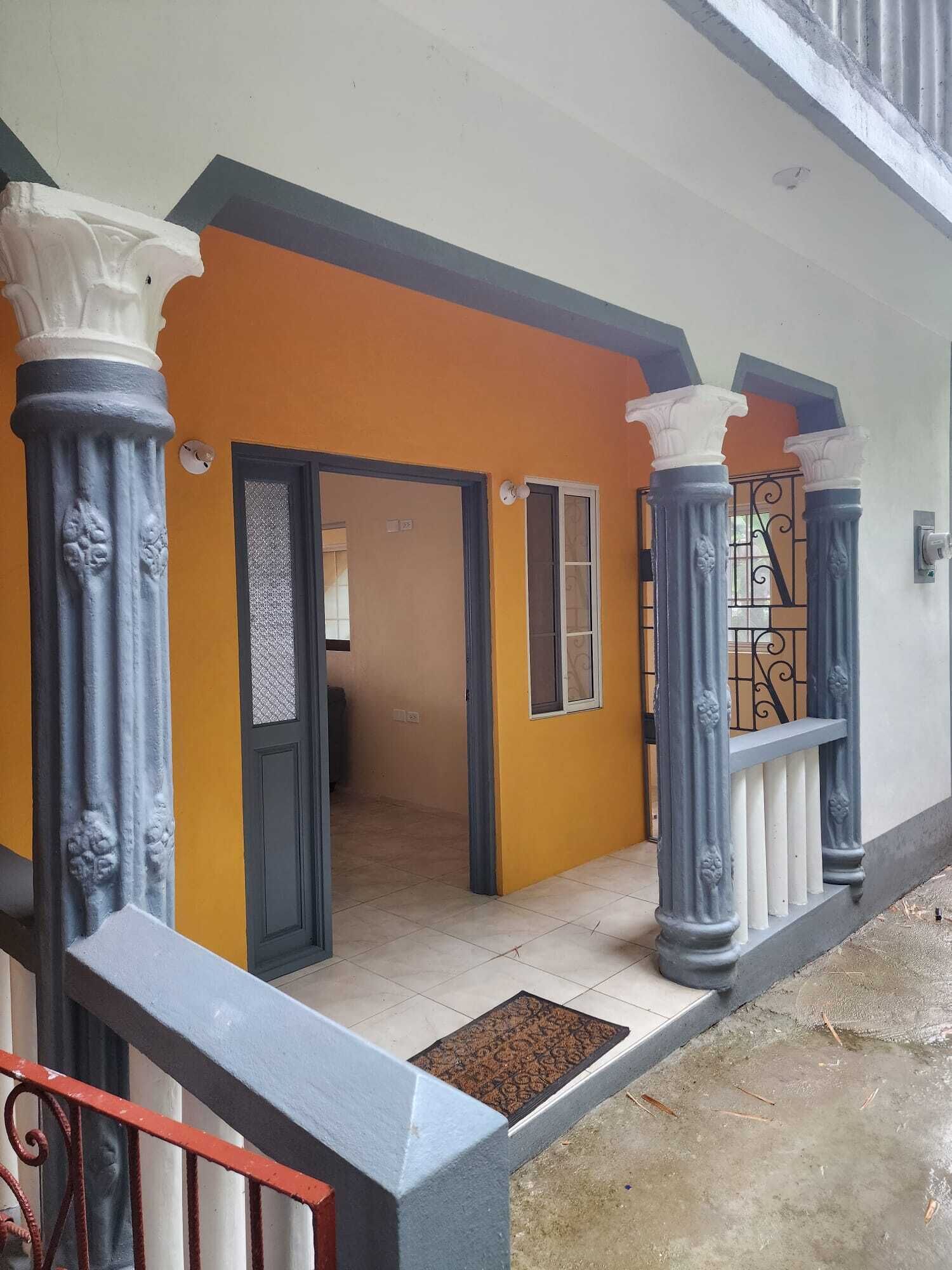 Fachada de un edificio con pared amarilla, columnas azules y una puerta de metal.