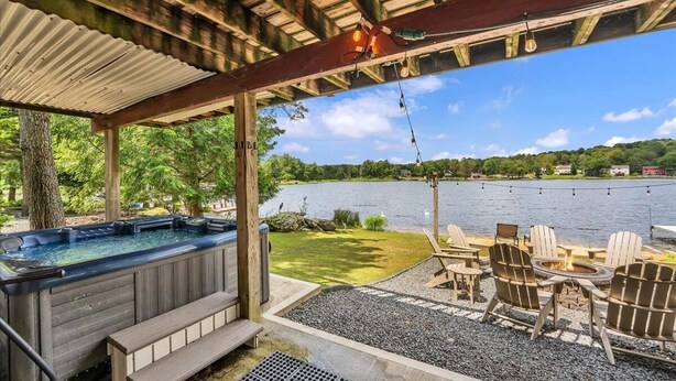 A hot tub and outdoor seating area with a view of a lake. - Amazing Lake Views, Game room, Private Beach, Hot Tub, Boats and Firepit (Tobyhanna)