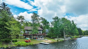 A lakeside cabin with a deck, dock, and boats. - Amazing Lake Views, Game room, Private Beach, Hot Tub, Boats and Firepit (Tobyhanna)