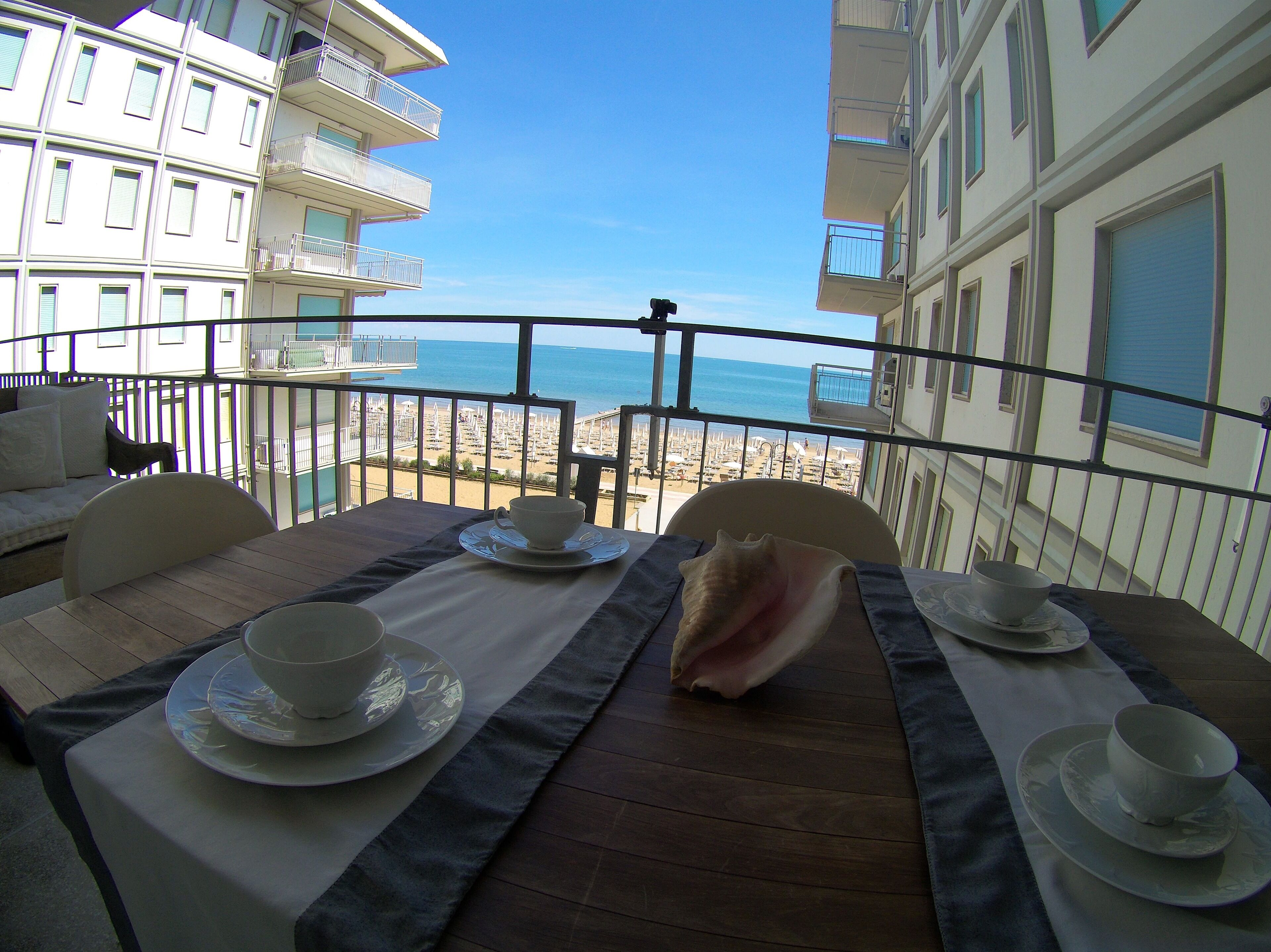 Een balkon met een tafel voor twee, met uitzicht op een strand met parasols en ligbedden.