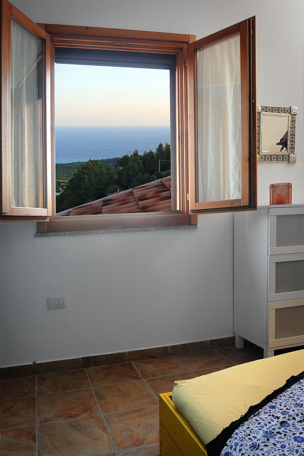 A bedroom with a large window overlooking a scenic view of the sea and greenery.